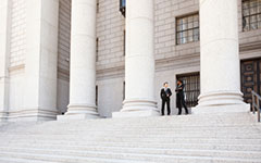 A well dressed man and woman converse on the steps of a legal or municipal building